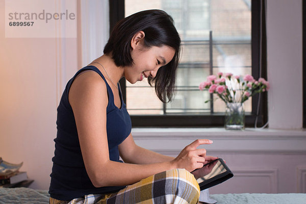 Junge Frau sitzt auf dem Bett und benutzt ein digitales Tablett