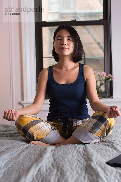Junge Frau auf dem Bett sitzend und meditierend