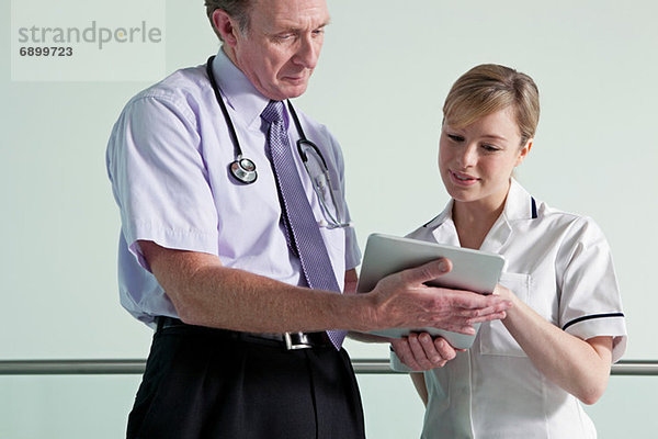 Arzt und Krankenschwester diskutieren über Krankenakten auf digitalem Tablett