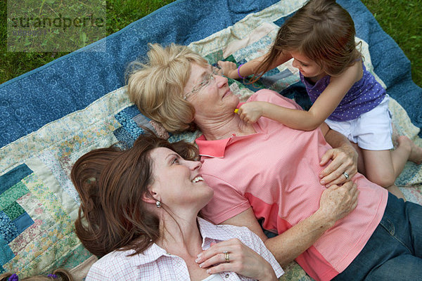 Drei Generationen Familie auf Picknickdecke liegend