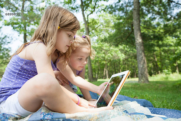Zwei Mädchen auf Picknickdecke mit digitalem Tablett sitzend