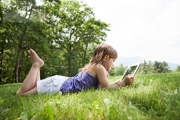Mädchen auf Gras liegend mit digitalem Tablett