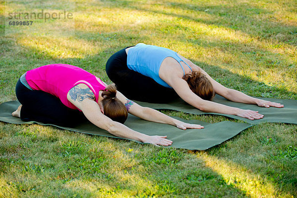 Zwei Frauen  die sich auf Yogamatten im Freien ausstrecken.