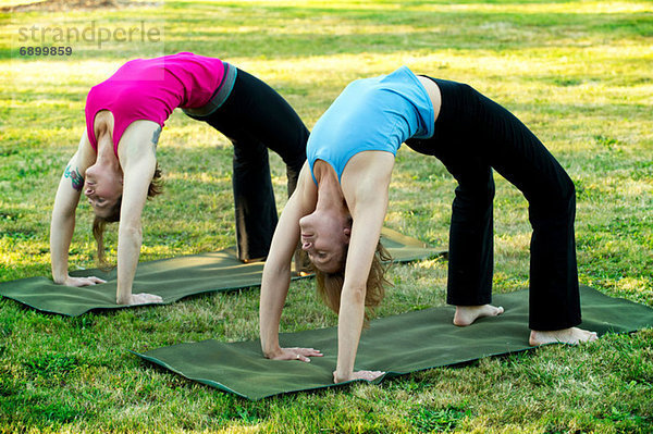 Zwei Frauen beugen sich auf Yogamatten im Freien nach hinten.