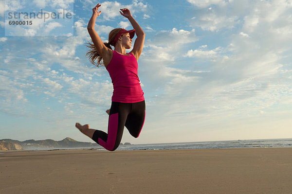 Junge Frau beim Springen in der Luft am Strand