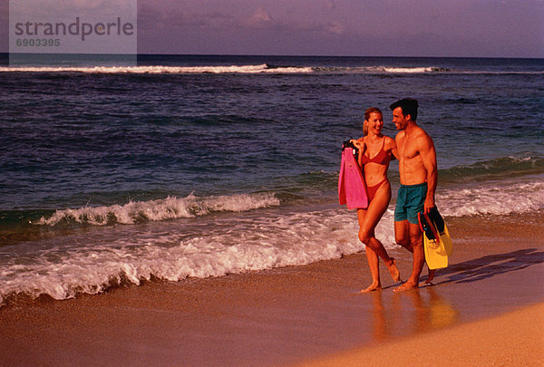 Couple in Swimwear  Walking on Beach Carrying Flippers