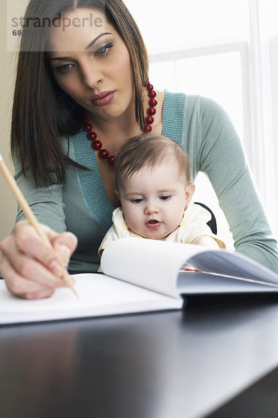 Mother Writing in Notebook  With Baby on Her Lap