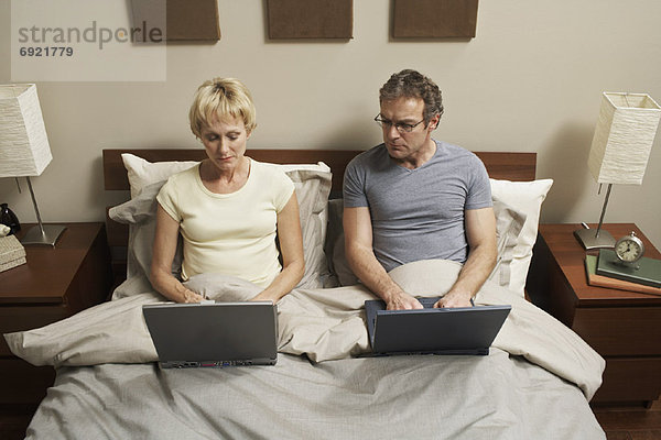 Paar mit Laptops im Bett