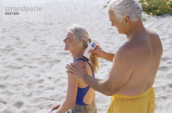 eincremen verteilen Mann Sonnencreme Frau auftragen Paar am Strand