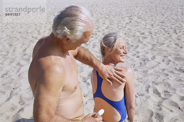 eincremen verteilen Mann Sonnencreme Frau auftragen Paar am Strand