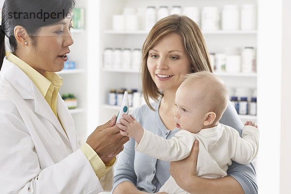 Pharmacist Holding Digital Thermometer  Talking to Mother With Baby