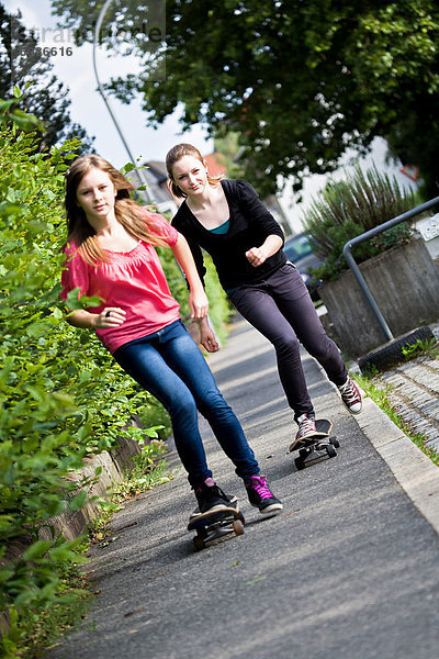 Zwei Mädchen  Teenager fahren Skateboard auf Bürgersteig