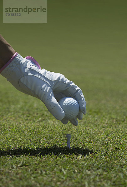 Golfball mit Handschuhen auf das Tee legen