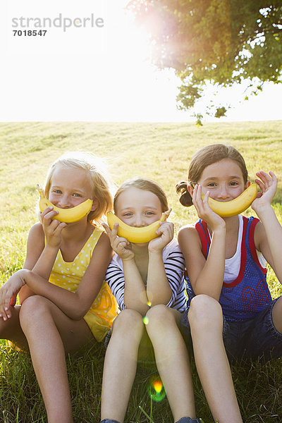 Mädchen halten Bananen über den Mund.