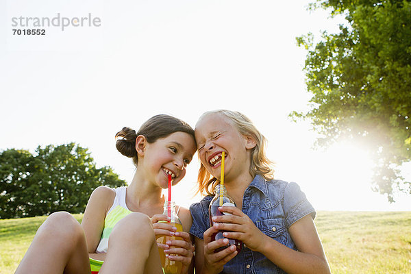 Lachende Mädchen trinken Saft im Freien