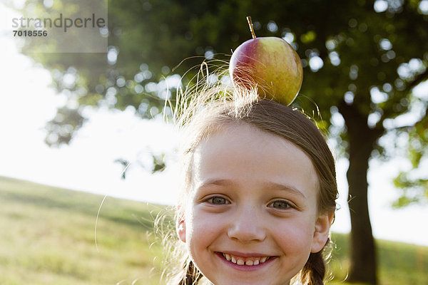 Lächelndes Mädchen balanciert Apfel auf dem Kopf