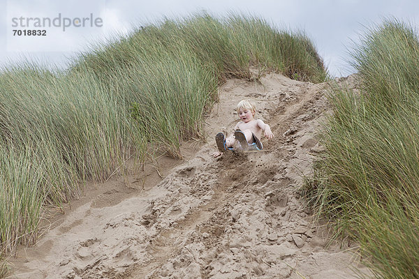 Junge rutscht die Sanddüne hinunter