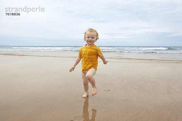 Junge geht in Wellen am Strand spazieren