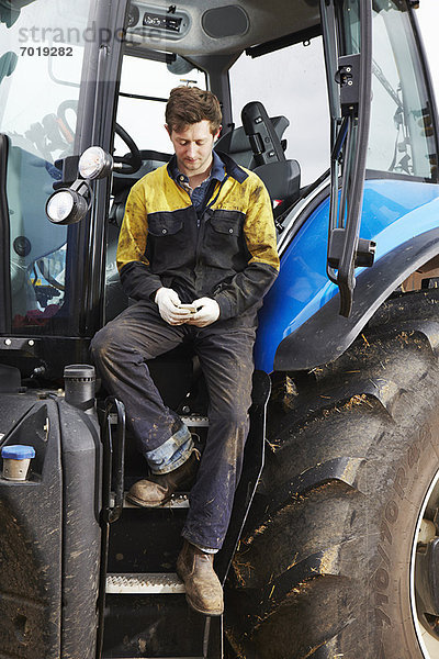 Landwirt mit Handy am Traktor