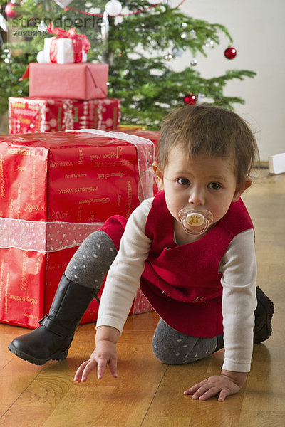 Kleines Mädchen vor Weihnachtsgeschenken kauernd