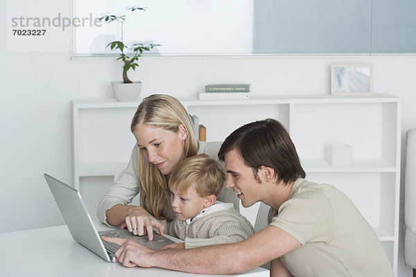 Eltern und kleiner Junge benutzen gemeinsam einen Laptop.