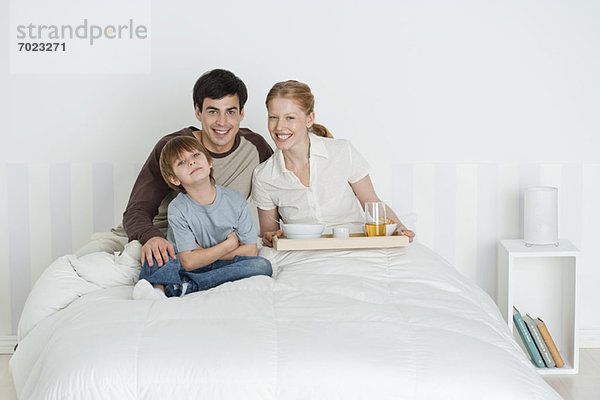 Junge Familie im Bett sitzend  Mutter mit Frühstückstablett