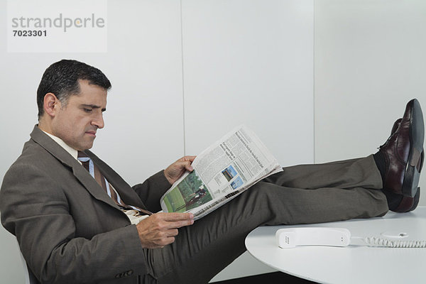 Geschäftsmann beim Zeitungslesen im Büro mit erhobenen Füßen auf dem Schreibtisch