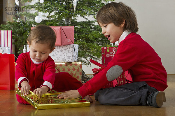 Junge hilft seiner kleinen Schwester beim Öffnen von Weihnachtsgeschenken