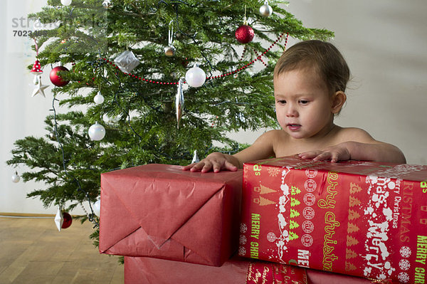 Baby Mädchen berührt gestapelte Weihnachtsgeschenke