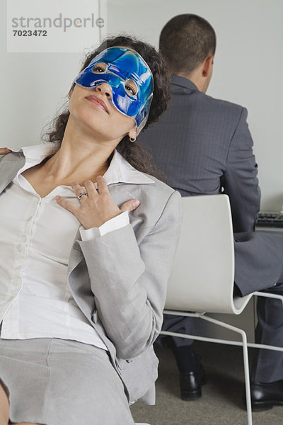 Frau entspannt mit Augenmaske im Büro als Kollegin arbeitet in der Nähe