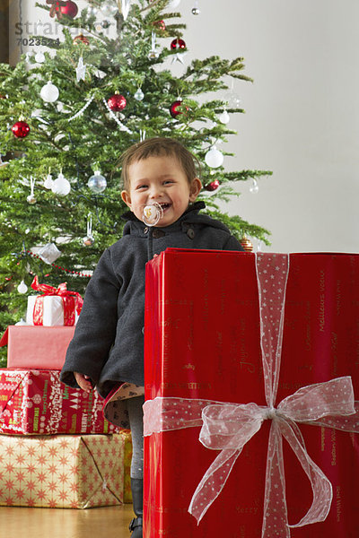 Kleines Mädchen steht hinter großem Weihnachtsgeschenk  lacht