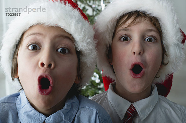 Jungen mit Weihnachtsmützen  die überraschte Gesichter machen.