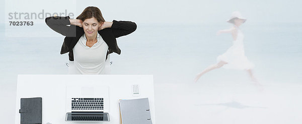 Reife Geschäftsfrau sitzt am Schreibtisch und stellt sich am Strand vor.