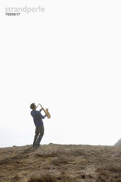 Mann  Steilküste  spielen  Saxophon