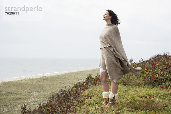 Junge Frau umwickelt Decke am Strand