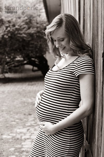 Lächelnde schwangere Frau vor einem Holztor  schwarzweiß