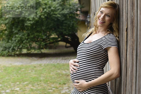 Lächelnde schwangere Frau vor einem Holztor