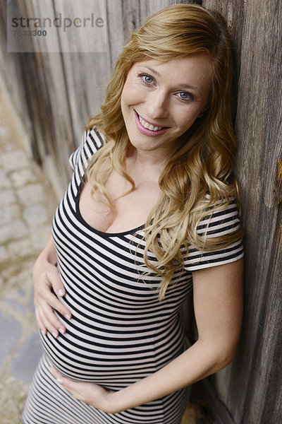 Lächelnde schwangere Frau vor einem Holztor