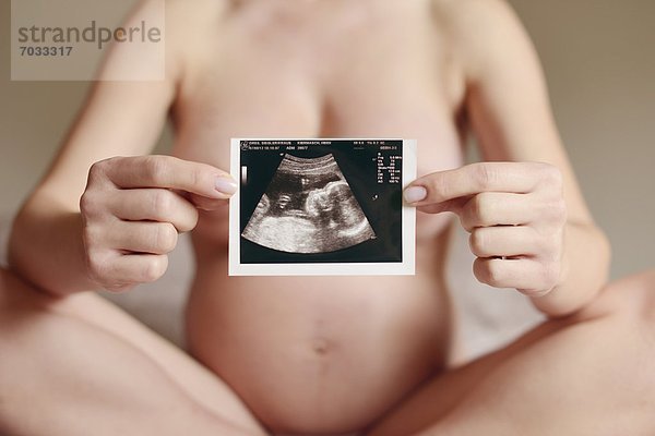 Nackte schwangere Frau zeigt Ultraschallbild