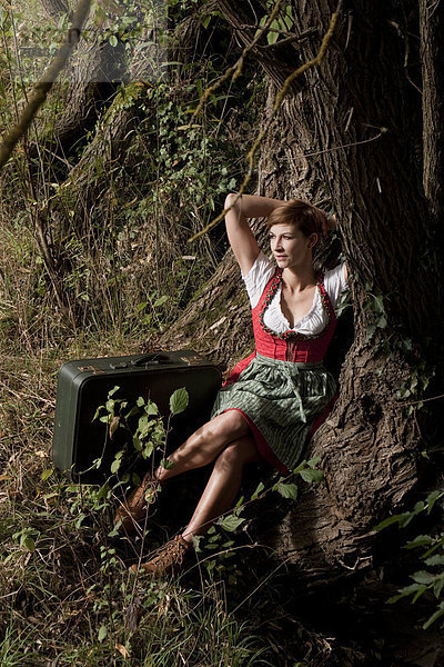 Frau im Dirndl sitzt an einem Baum