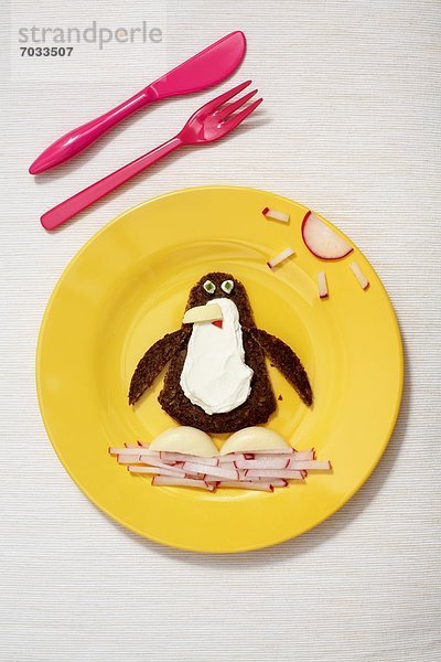 Kinderteller mit Vollkornbrot  Frischkäse und Radieschen in Form eines Pinguins