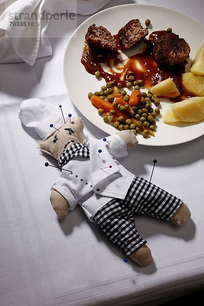 Voodoo-Puppe eines Kochs mit Stecknadeln auf gedecktem Tisch neben dem Essen