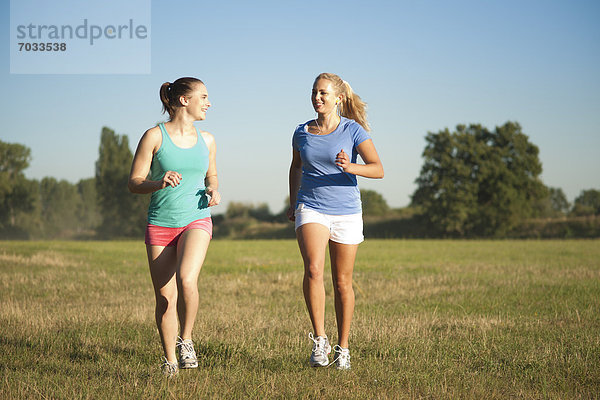 Zwei junge Frauen joggen auf einer Wiese