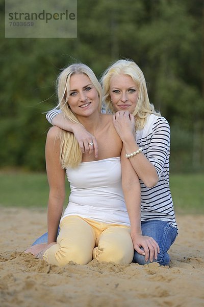 Zwei fröhliche blonde junge Frauen am Sandstrand