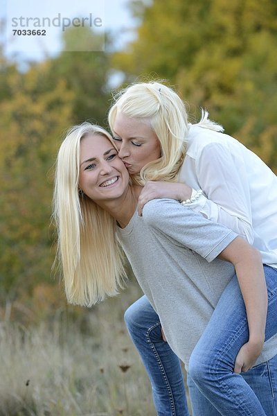 Fröhliche blonde junge Frau trägt ihre Freundin huckepack