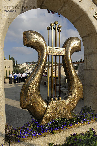 Skulptur einer Davidsharfe am Eingang der Davidstadt  einer archäologischen Ausgrabungsstätte  dahinter eine jüdische Besuchergruppe und ein palästinensisches Dorf  Ostjerusalem  Jerusalem  Israel  Vorderasien  Naher Osten