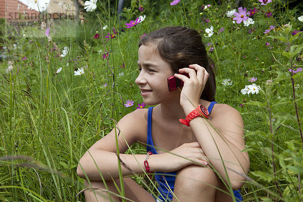 Mädchen  11 Jahre  telefoniert inmitten einer Blumenwiese in freier Natur
