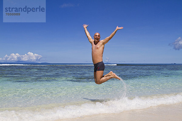 Mann  45 Jahre  macht vor Freude einen Luftsprung am Strand  Insel La Digue  Seychellen  Afrika  Indischer Ozean
