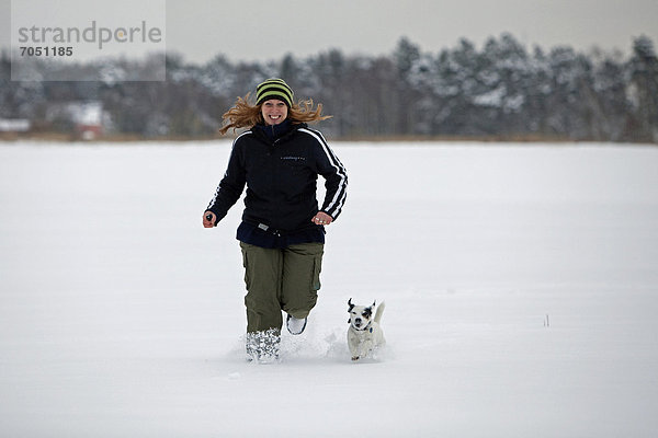 Ein Frau läuft mit ihrem kleinen Hund durch den tiefen Schnee