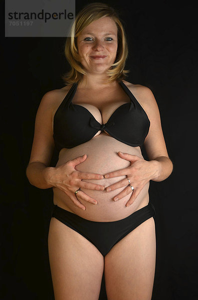 Schwangere junge Frau mit Babybauch  9. Monat  streichelt sich Bauch